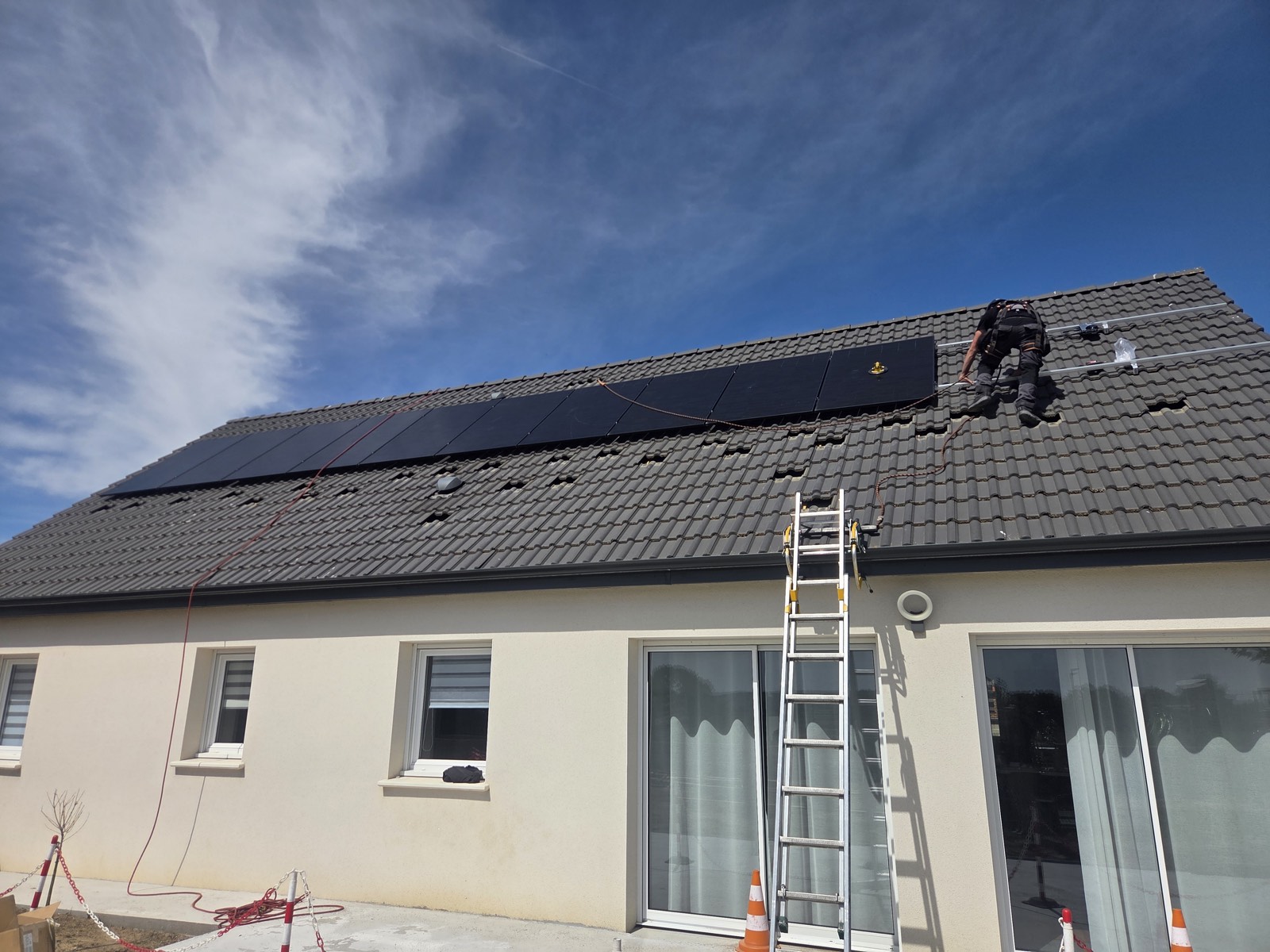 Un installateur pose des modules photovoltaïques en surimposition sur une toiture en tuiles.